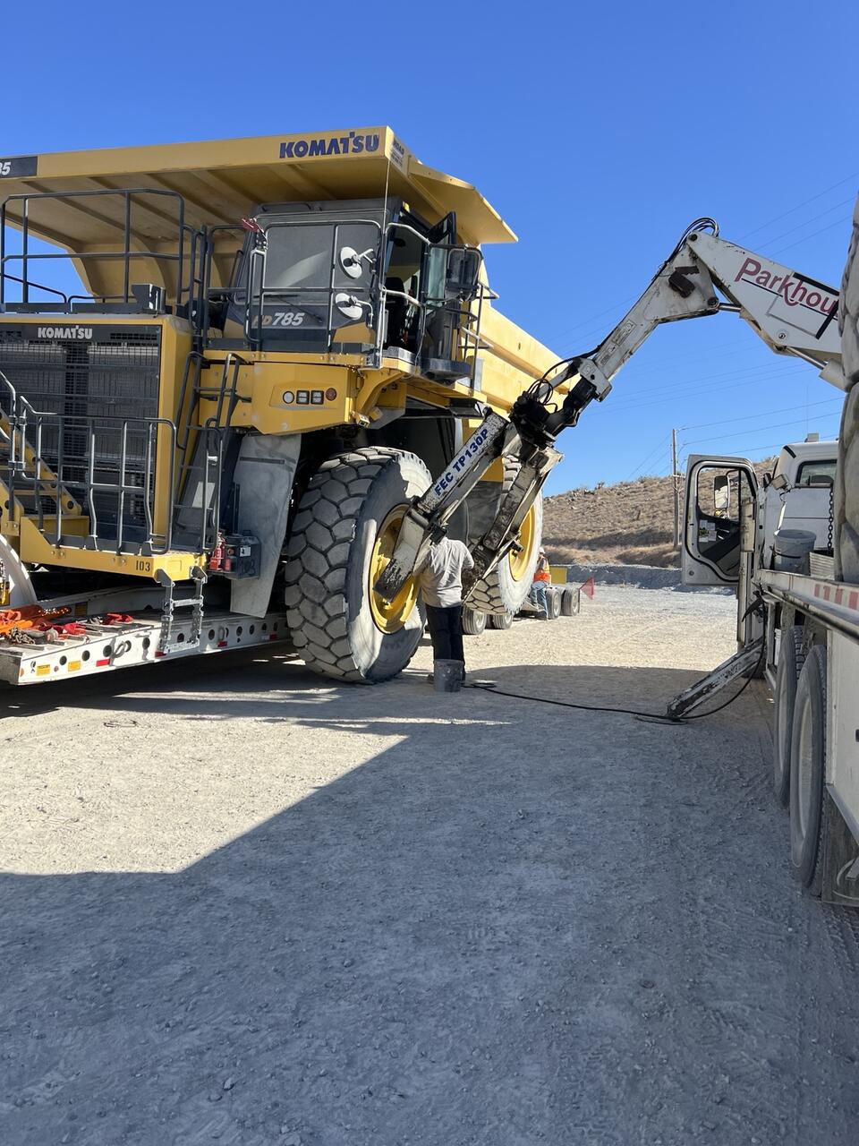 Crew removing a rear tire from the Komatsu HD785 with a telehandler tire manipulator during loading