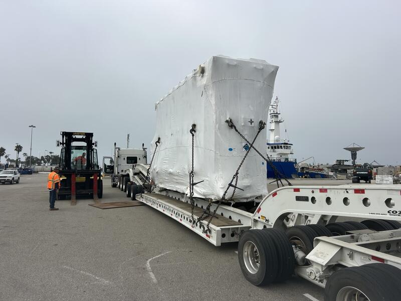 Crew member and forklift standing by as the wrapped power transformer is secured with chains at the Port of Long Beach